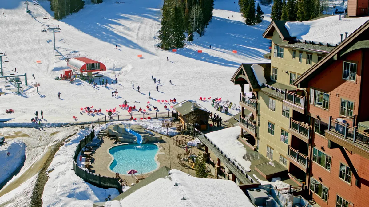 An inviting exterior view showing ski slopes, a swimming pool, ski lifts, the lodge building, and a snow-covered landscape bustling with activity. People are seen skiing and socializing, giving a lively, festive vibe that extends the sense of après-ski enjoyment.