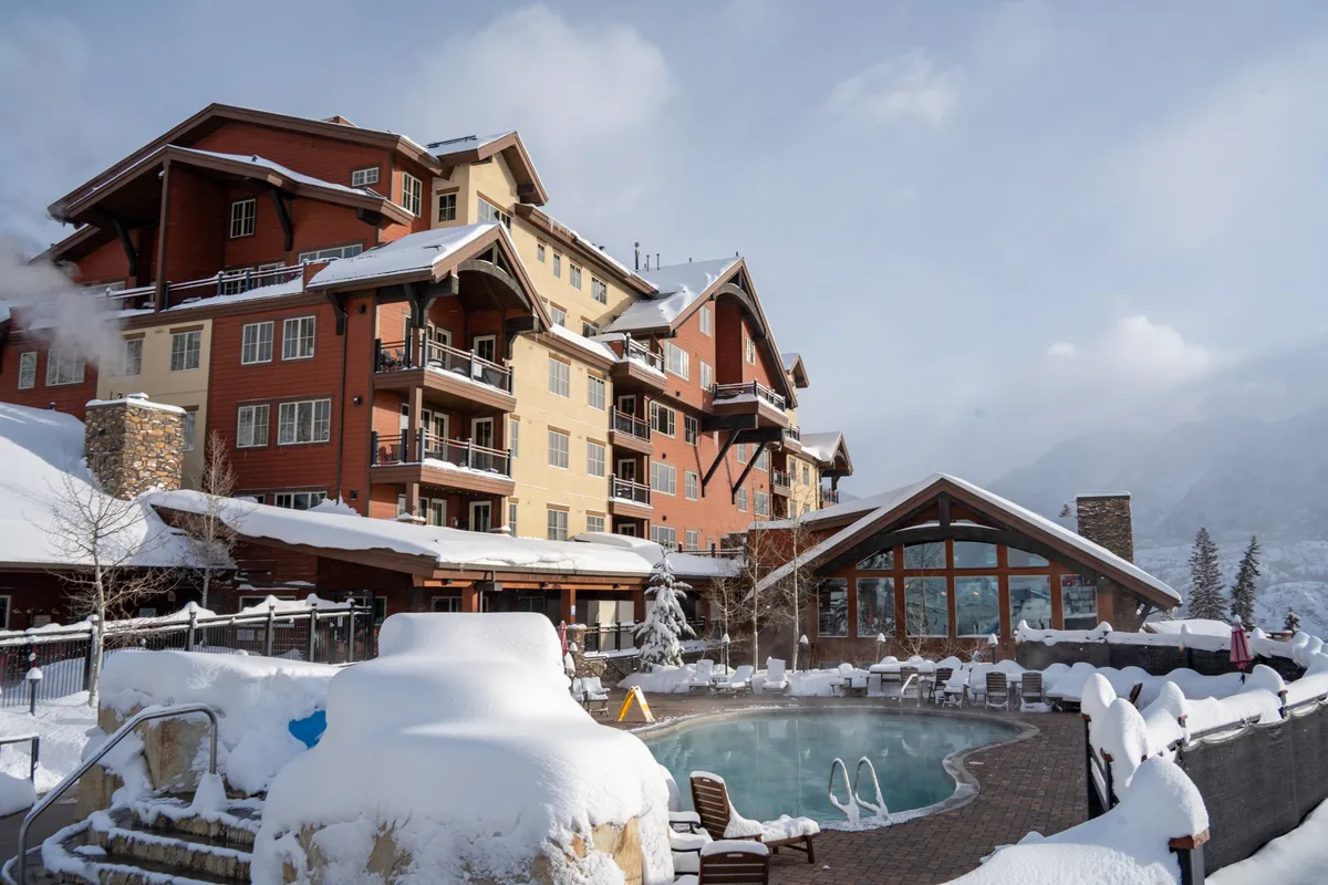 This image captures a snow-covered, heated swimming pool set against a multi-story lodge and snow-laden trees. The tranquil wintry setting hints at the warmth and comfort of year-round swimming, even in the midst of a snowy landscape. Lounge chairs and the cozy ambience add to the sense of resort-style indulgence.