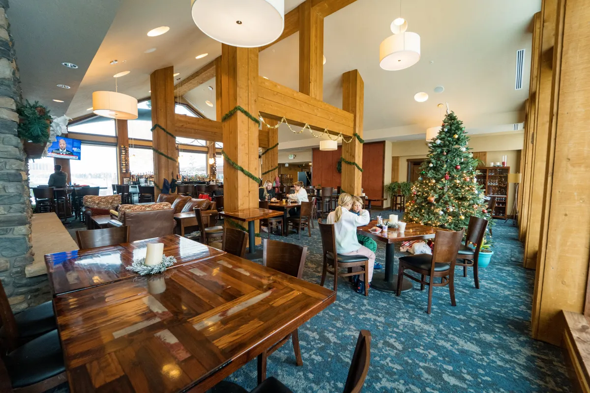 A festive, open seating area with a prominent Christmas tree, comfortable couches, and a bar area. The setting feels lively yet cozy, suggesting a welcoming spot for gathering after outdoor adventures or during special events.