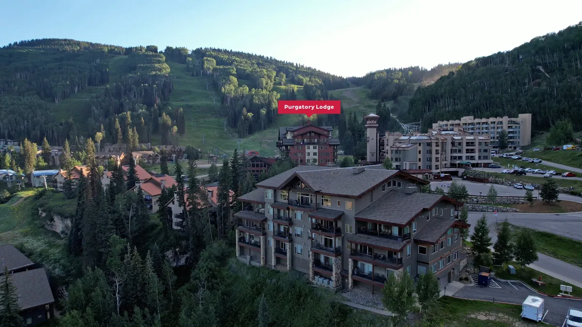 A panoramic view of Purgatory Lodge set against the majestic San Juan Mountains, with nearby buildings and a hint of the bustling outdoor life. The setting suggests close access to both natural trails and resort amenities.