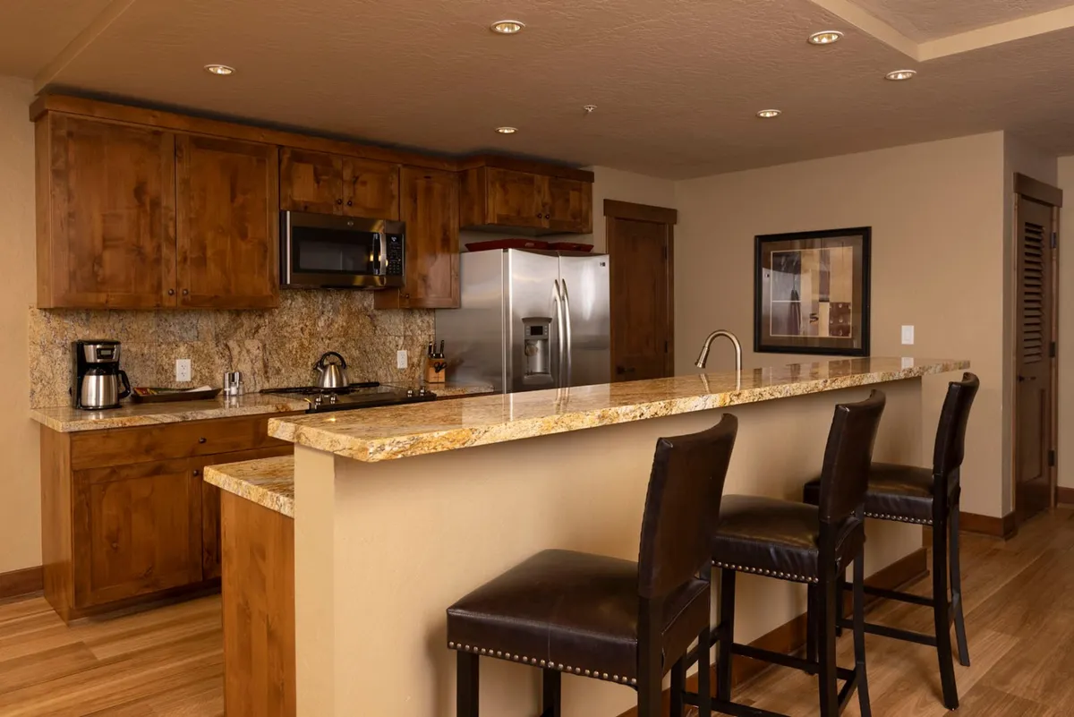 This image showcases a modern kitchen with a prominent granite countertop, complemented by stools for casual seating. Visible appliances, including a coffee maker, contribute to a lived-in and functional atmosphere, while the presence of artwork adds a personal touch. The open layout hints at easy movement between kitchen, dining, and living spaces, supporting social interaction.