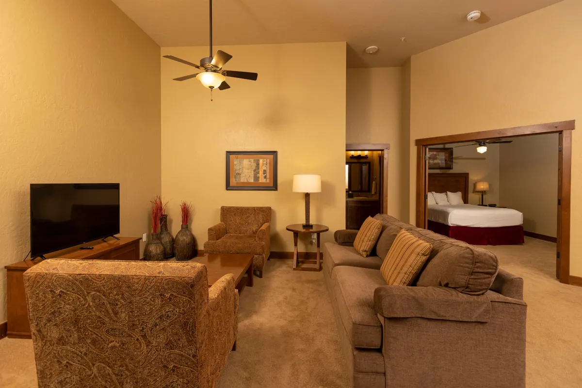 A comfortable loft living area featuring a sofa and armchairs around a coffee table, with a television at the focal point and a warm, inviting ambiance. The arrangement is perfect for relaxing, watching TV, or hanging out as a group, capturing the loft's flexibility as a teen or guest hideaway.