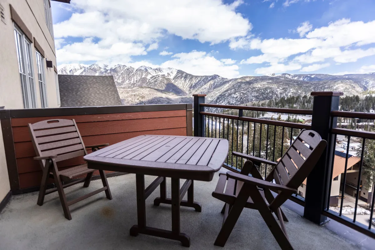 The image showcases an inviting outdoor dining area with a table and chairs set on a spacious balcony, overlooking breathtaking mountain vistas. The setting suggests a peaceful environment perfect for relaxing, enjoying morning coffee, or unwinding with a book, all while surrounded by the natural beauty of Durango's mountains.