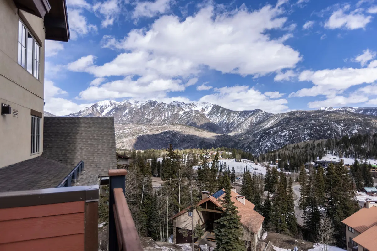 A breathtaking view of the mountain range and pine forests, as seen from an elevated vantage point, possibly a balcony. The distant cabins and layers of peaks evoke the pristine, tranquil setting outside, hinting at the scenic vistas enjoyed from inside the property.
